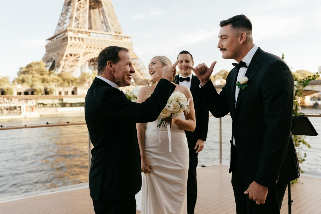 during a paris wedding ceremony taking place on a boat, the father of the bride and the groom are exchanging a personalised hello sign, during their personalised wedding ceremony by a paris officiant